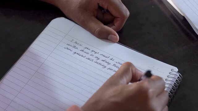 Close-up of a person writing by hand in a notebook at a desk, capturing a quiet moment of writing, planning, journaling, or personal reflection
