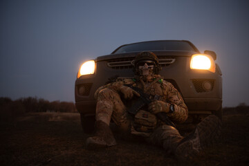 Man in camouflage sitting in front of an off-road vehicle at dusk © Mykola Stotskiy