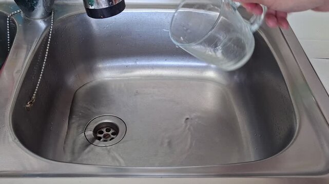 Water is poured into a stainless steel sink from a cup while it flows down the drain. The process repeats to show the movement