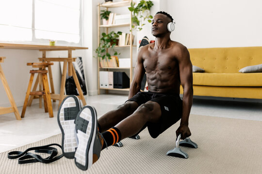Man performing l-sit calisthenics workout on parallettes in modern living room, focusing on strength and fitness