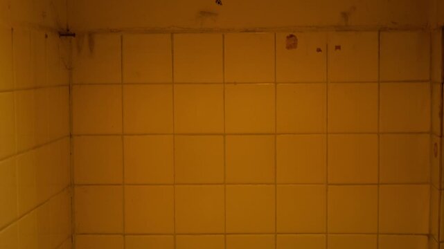 Grungy Yellow-Stained Bathroom Tile Wall Corner with Old Plumbing, Weathered Interior Texture