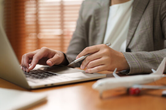 Businesswoman works on a laptop beside an airplane model, representing air freight, global shipping, supply chain management, cargo transportation, airline booking and international logistics.