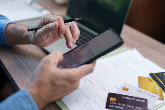 Man uses a smartphone calculator beside credit cards and financial documents, representing credit payment, debt management, household budgeting