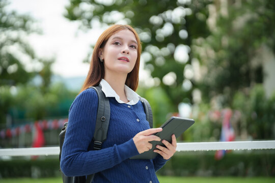 Young female university student holding a digital tablet outdoors on campus, representing modern education, confidence, technology, and an active academic lifestyle.