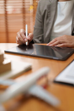 Businesswoman uses digital tablet and stylus beside an airplane model and parcel, representing digital travel planning, airline booking, air freight