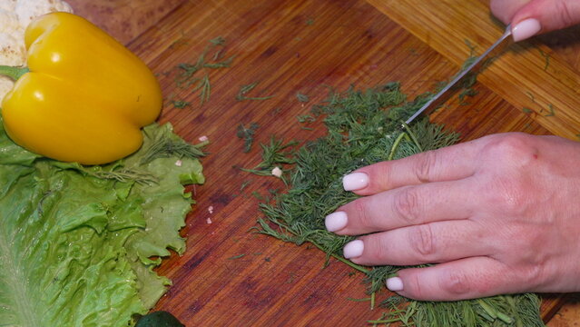 Dill vegetable chopping cutting board cooking fresh herbs being sliced by female hands on a wooden surface for healthy salad preparation