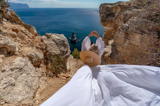 Woman ocean cliffs girl standing on rocky edge wearing white dress and sun hat enjoying panoramic sea view during summer vacation