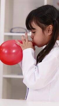 Young Girl in Lab Coat Blowing Up a Red Balloon