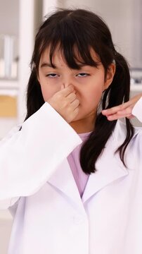 Young Girl in Lab Coat Pinching Nose at Bad Smell