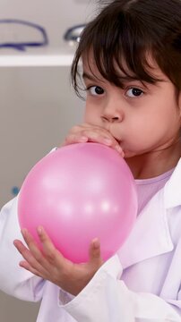 Young Girl in Lab Coat Blowing Up Pink Balloon