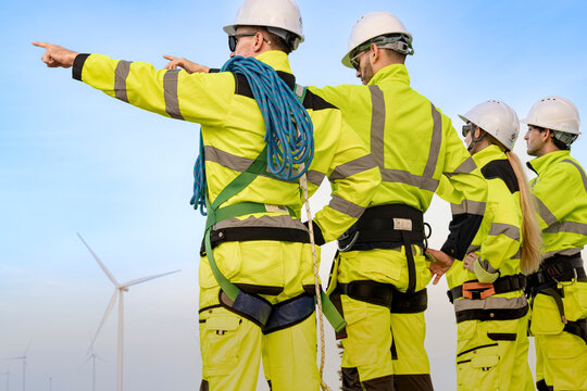 Back view of four clean power workers as the front technician raises his arm to full stretch and his bearded colleague turns to catch the given direction during a site walk