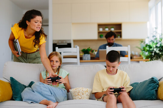 Frustrated mother scolding children playing video games, capturing modern family conflict over screen time, parenting struggles and digital addiction at home