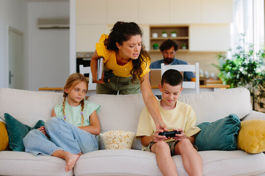 Mother feeling frustration while interrupting her children's gaming session on the couch, highlighting parenting challenges, screen time management, and family dynamics in a modern home environment