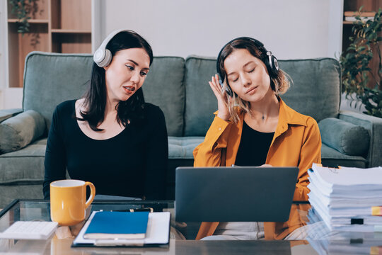 Two young female students using a laptop while sitting on a sofa at home. Student life concept with studying, teamwork, and online learning.