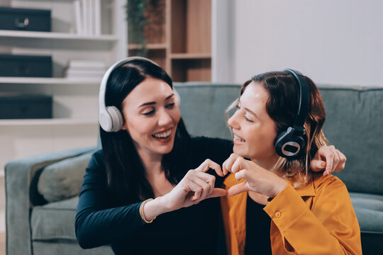 Two young female students using a laptop while sitting on a sofa at home. Student life concept with studying, teamwork, and online learning.