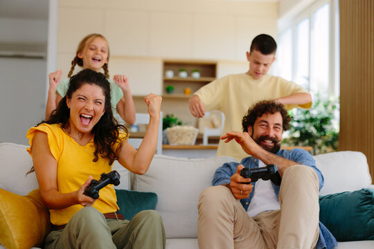 Happy parents and children bonding while enthusiastically playing a video game in their living room, celebrating wins and experiencing joyful excitement together