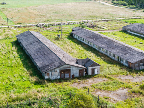 Aerial view of abandoned Soviet-era agricultural buildings with weathered roofs and overgrown fields in a rural landscape, Kulciems, Talsi Municipality, Latvia.