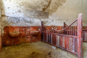 Stone feeding troughs and red stall gates in an old vaulted horse stable © Michal Plevko