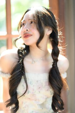 Young Woman with Long Wavy Hair and Soft Smile Near Sunlit Window