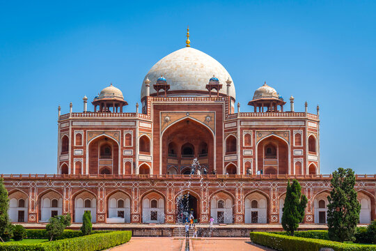 Majestic red sandstone Mughal architecture featuring a large white marble dome and water fountain under clear blue sky at Humayun's Tomb, Delhi, India.