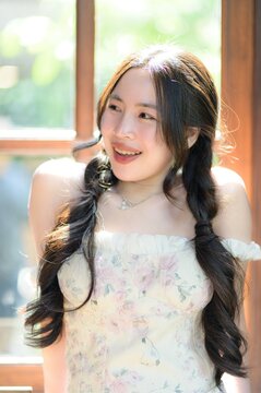 Smiling young woman with long dark hair in a floral dress enjoying sunlight indoors
