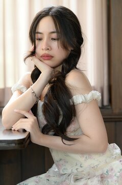 Young woman with long dark hair resting her chin on hand indoors