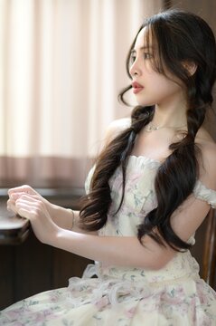 Young woman playing piano beside window with natural light in a living room