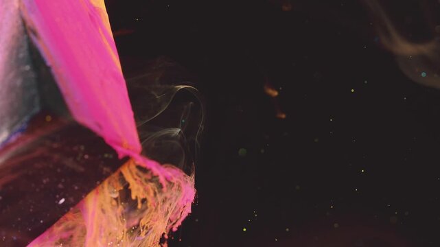 Tight macro view of thick pink and orange paint smeared on textured surface at left with visible drips, strands, and wet gloss while translucent smoke or ink wisps curl