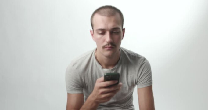 Rack Focus Shot of Young Man with Smartphone Looking at Camera on White Background