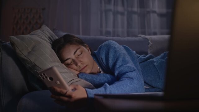 Caucasian young adult woman lying on sofa, staring blankly at smartphone screen with exhausted expression. Clip represents digital burnout, perfect for mental health and wellness campaigns