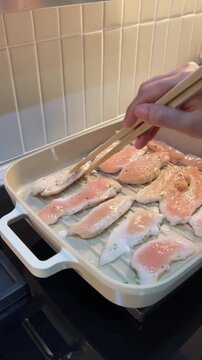 Hand cooking healthy food fresh chicken breast fillet slices using wooden tong on grill pan in domestic kitchen, preparing meal with calm focus