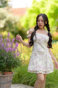 Young woman in floral dress in garden with purple flowers on a bright sunny day