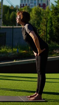 Focused outdoor forward-bend yoga practice on green lawn with woman stretching hamstrings and spine alignment against blurred urban residential backdrop