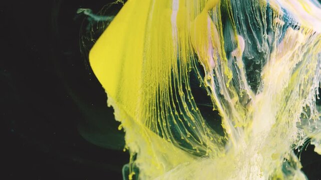 Close-range macro scene of thick lemon-yellow and pale cream paint stretching downward through dark teal-black liquid with glossy ripples and suspended details