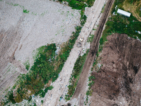 Aerial view of a municipal solid waste landfill with heavy machinery operating on a dirt path amidst sorted waste piles and surrounding greenery in Laidzes pagasts, Talsu novads, Latvia.