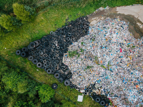 Aerial view of a large pile of discarded black tires adjacent to a waste dump site surrounded by green grass and trees in Laidzes pagasts, Talsu novads, Latvia.