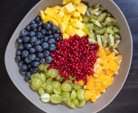 Fruit salad with kiwi, oranges, pineapple, blueberries, grapes, and pomegranate seeds in a bowl. Sweet food, healthy eating, organic, ripe, prepearing salad, ready to eat.