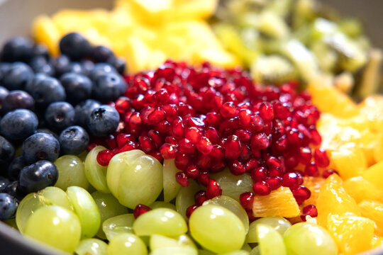Close-up of blueberries, grapes, oranges, and pomegranate seeds in a bowl for a fruit salad. Sweet foods, healthy eating, organic, ripe, preparing a salad, ready to eat.