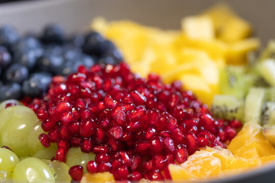 Close-up of blueberries, grapes, oranges, and pomegranate seeds in a bowl for a fruit salad. Sweet foods, healthy eating, organic, ripe, preparing a salad, ready to eat.