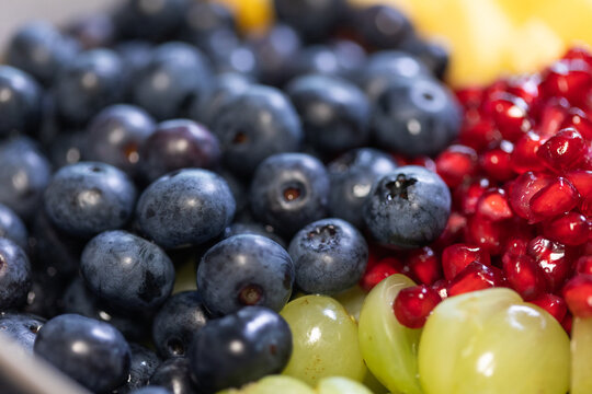 Close-up of blueberries, grapes, oranges, and pomegranate seeds in a bowl for a fruit salad. Sweet foods, healthy eating, organic, ripe, preparing a salad, ready to eat.
