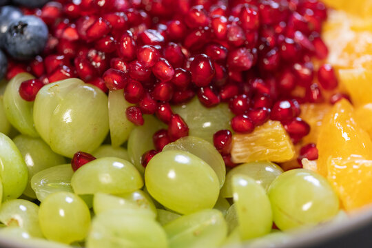 Close-up of grapes, oranges, and pomegranate seeds in a bowl for a fruit salad. Sweet foods, healthy eating, organic, ripe, preparing a salad, ready to eat.