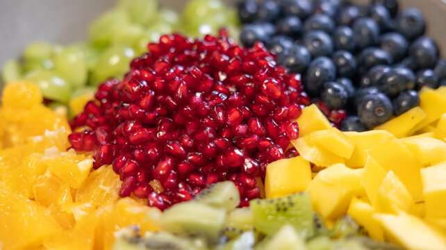 Close-up of kiwi, pineapple, blueberries, grapes, oranges, and pomegranate seeds in a bowl for a fruit salad. Sweet foods, healthy eating, organic, ripe, preparing a salad, ready to eat.
