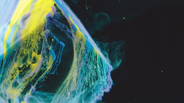 Cinematic close-up of colorful pigment plumes suspended in dark medium showing thick cyan and yellow masses peeling and thinning into translucent lace-like filaments