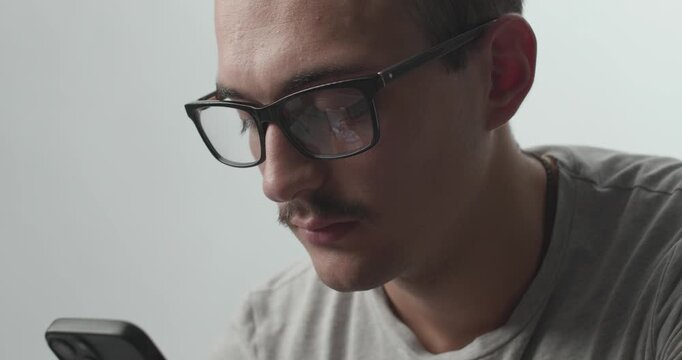 Close-up of Young Man with Glasses Focused on Smartphone with Screen Reflection