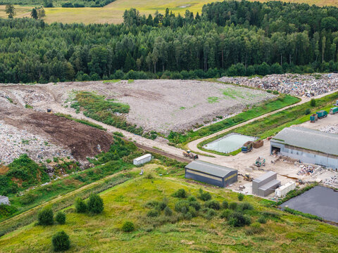 Aerial view of a municipal solid waste landfill with waste processing facilities, sorting areas, and surrounding green fields and forests in Laidzes pagasts, Talsu novads, Latvia.