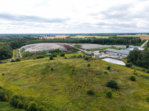 Aerial view of a municipal solid waste landfill with processing facilities, waste piles, and surrounding forest in Laidzes pagasts, Talsu novads, Latvia.