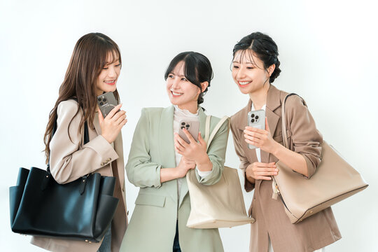 スマートフォンを手に談笑する仲の良いビジネスウーマン3人