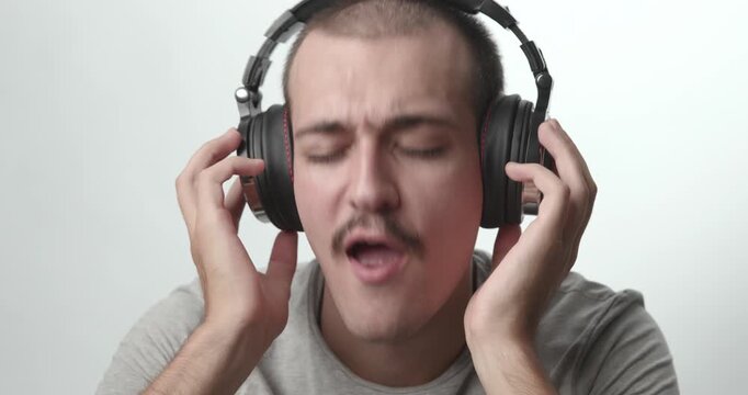 Close-up of Young Man Wearing Headphones Singing and Enjoying Music on White Background