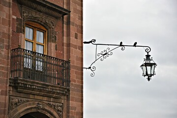 Naklejka premium Antique cast iron wall lantern on a Colonial building stone wall in San Miguel de Allende, Guanajuato Mexico.