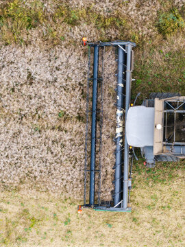 Aerial view of a combine harvester harvesting a rapeseed field with mechanical header cutting through the crop in Talsi Municipality, Latvia.